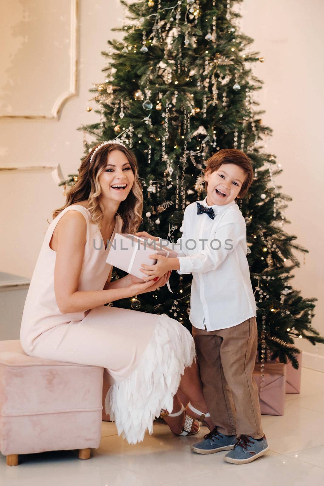 Mom gives her son a Christmas present near the Christmas tree.Happy family by Lobachad