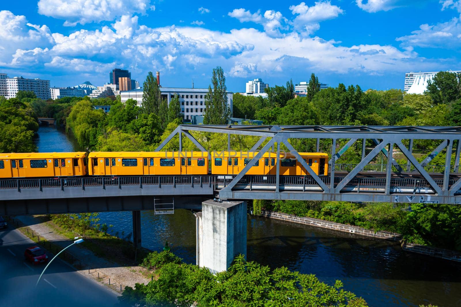A bright yellow passenger train rides across a bridge over a river.