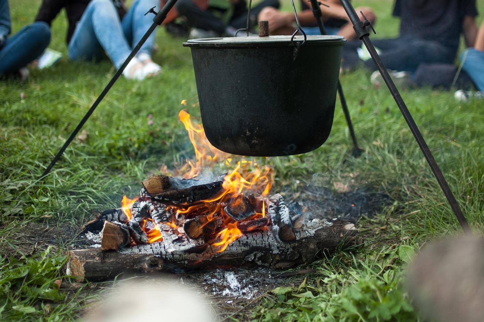 Dark big pot or cauldron, cooking pan with boiling water inside above the fire somewhere in the park or mountains, camping concept.