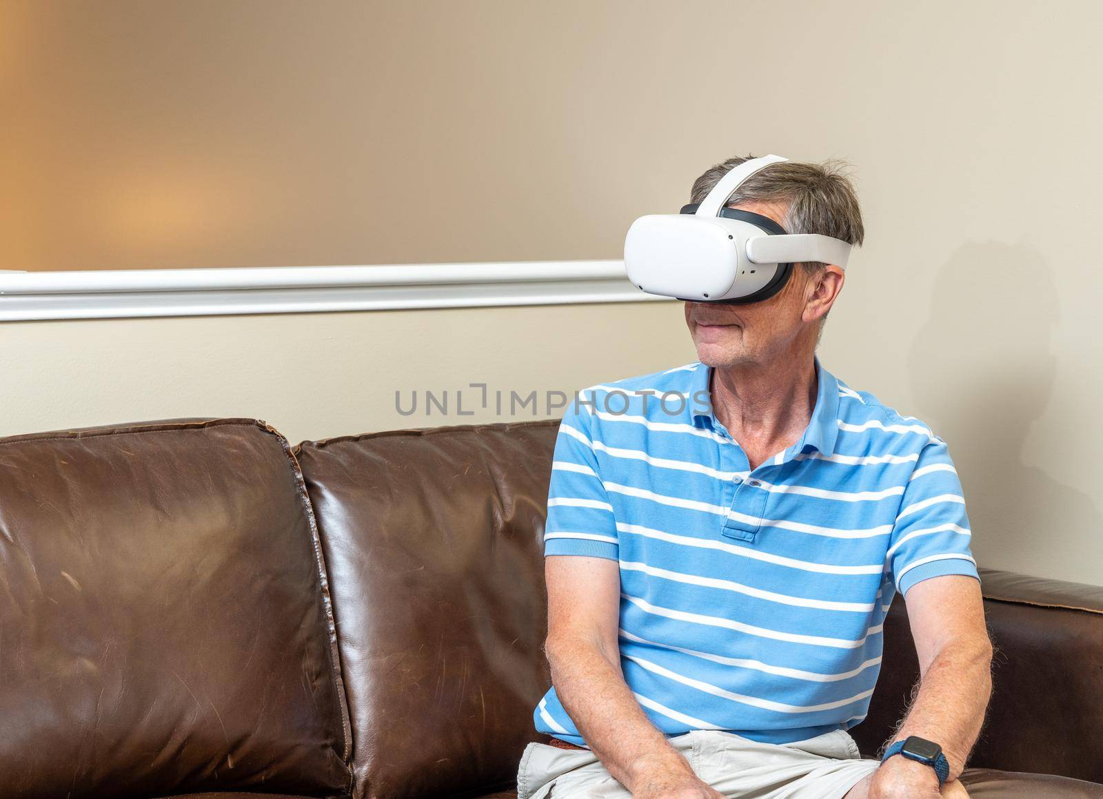 Senior man seated and watching an app on a modern virtual reality VR headset in home