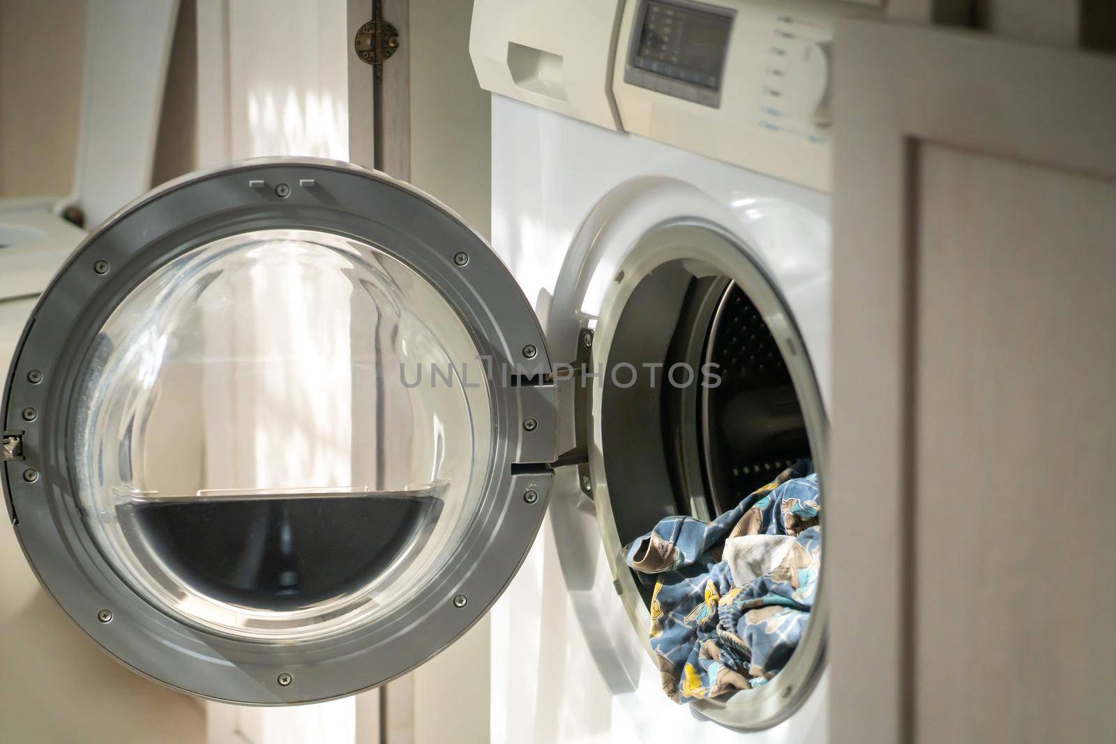 White washing machine with open door and linen inside, cleaning and washing clothes in the laundry room, at home in the bathroom.