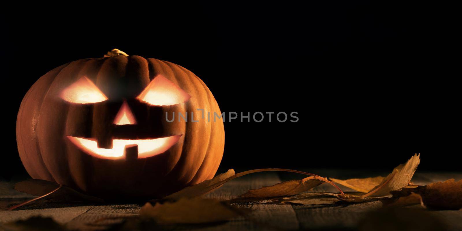 Halloween pumpkin head jack lantern with glowing eyes on wooden table.