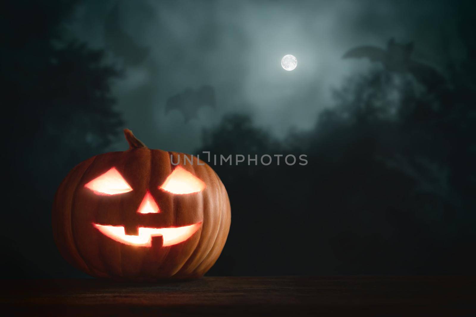 Halloween pumpkin head jack lantern with glowing eyes on a wooden table in the moonlight.