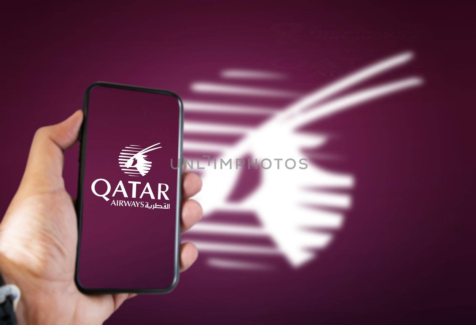 Doha, Qatar, July 2021: A hand holding a phone with the Qatar Airways airline app on the screen and the arabian oryx logo blurred on a dark cherry background.