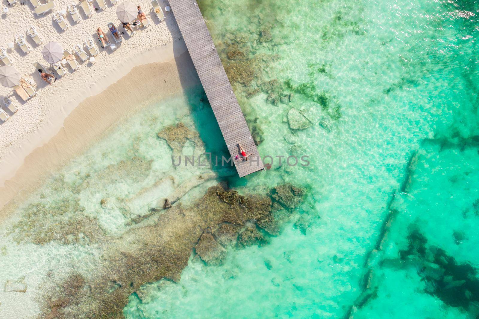 Aerial high top view of woman laying on wooden pier at sunny summer day in Cancun, Mexico, top view. Young sexy woman in red swimsuit in summertime in Caribbean. Summer beach vacation concept