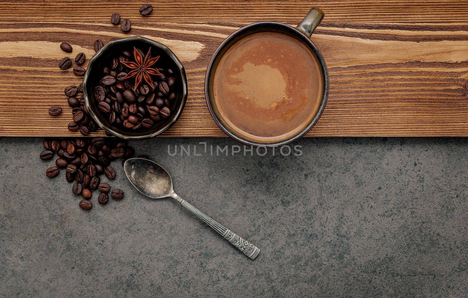 Roasted coffee beans with coffee cup setup on dark stone background.