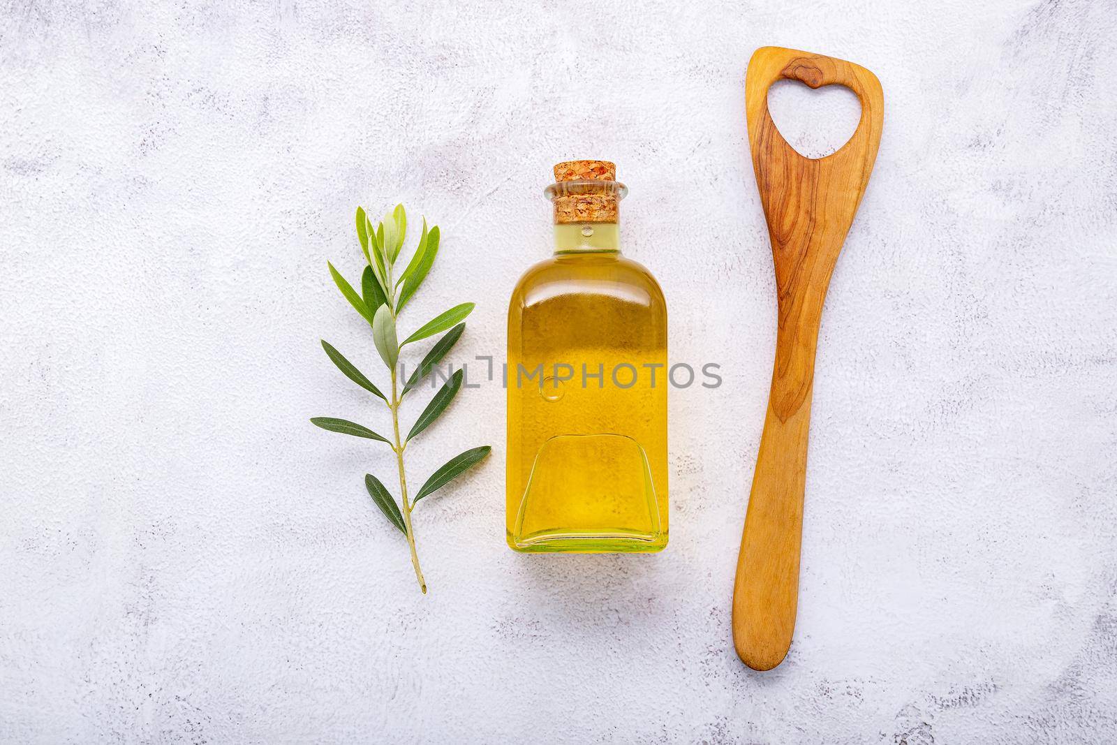 Glass bottle of olive oil and olive branch set up on white concrete background.