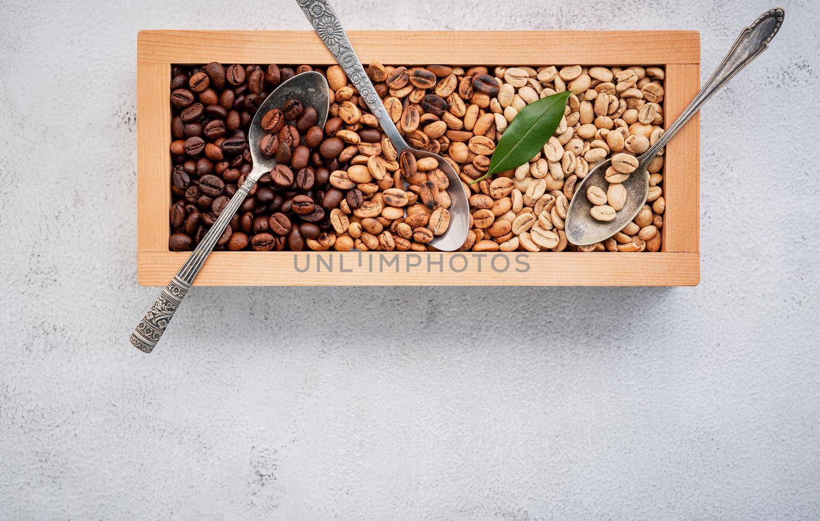 Green and brown decaf unroasted and dark roasted coffee beans in wooden box with scoops setup on white concrete background. with scoons setup on white concrete background. by kerdkanno