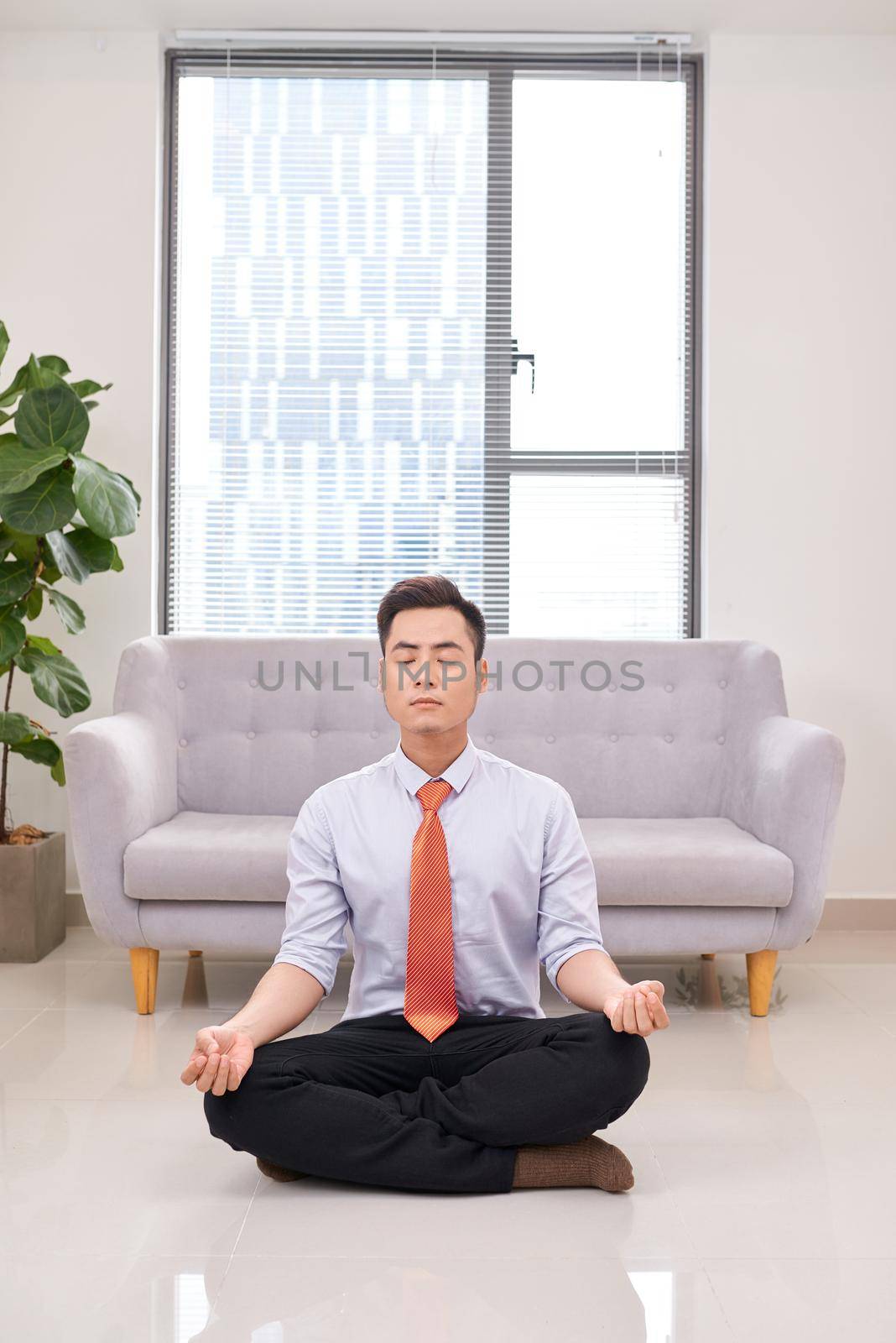 Businessman meditating in lotus pose on the floor in the office 