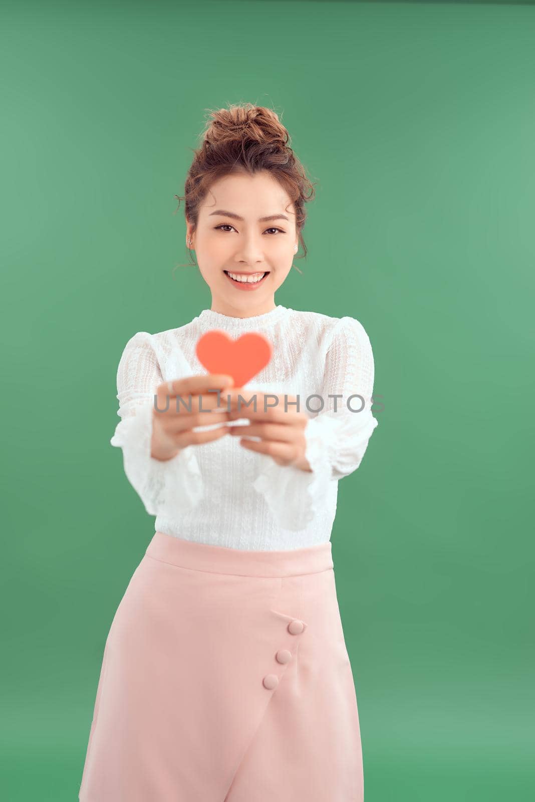 Cheerful young Asian woman holding red heart paper isolated over green background.  by makidotvn