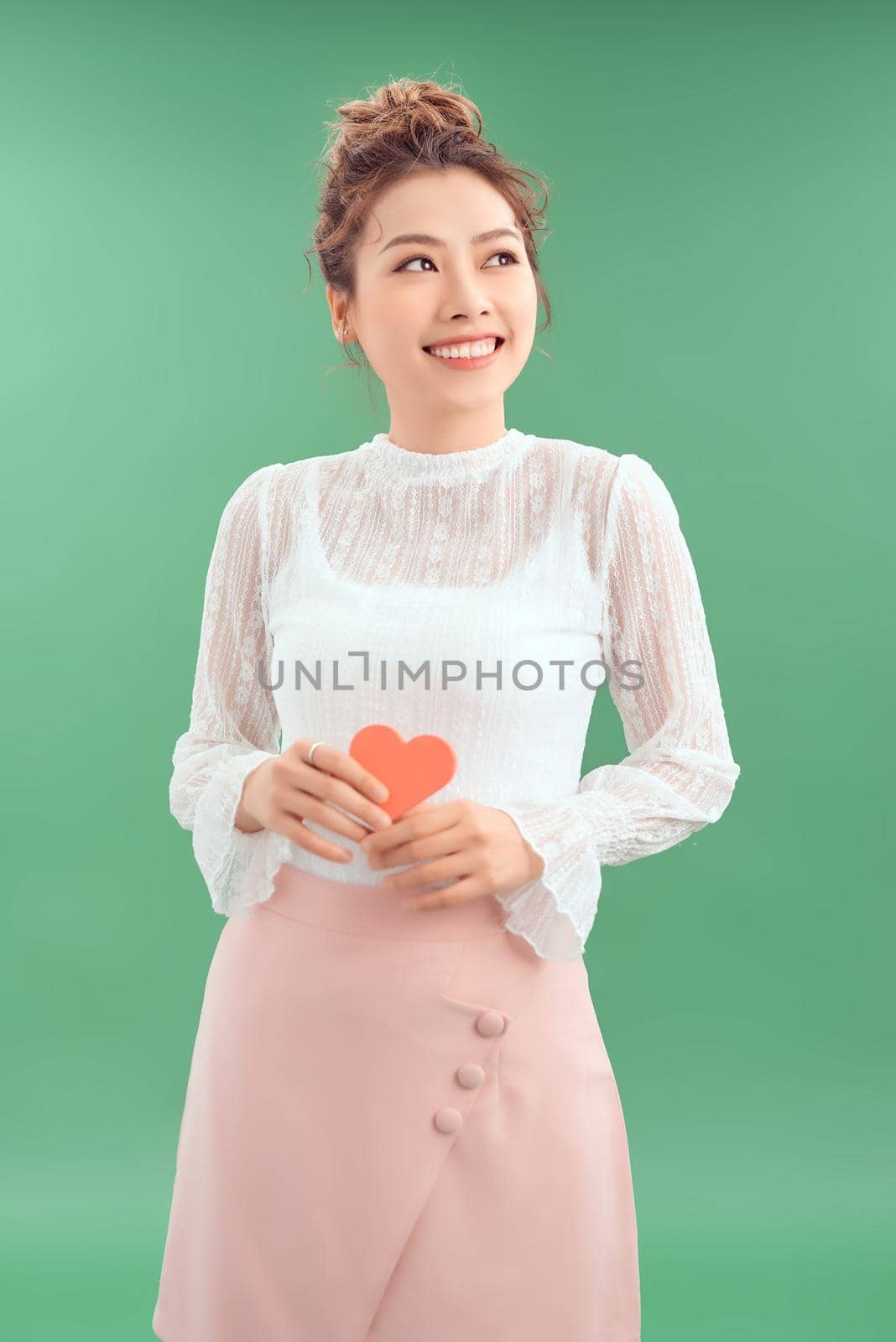 Asian Woman holding paper heart shaped card over green background. Valentine day concept.