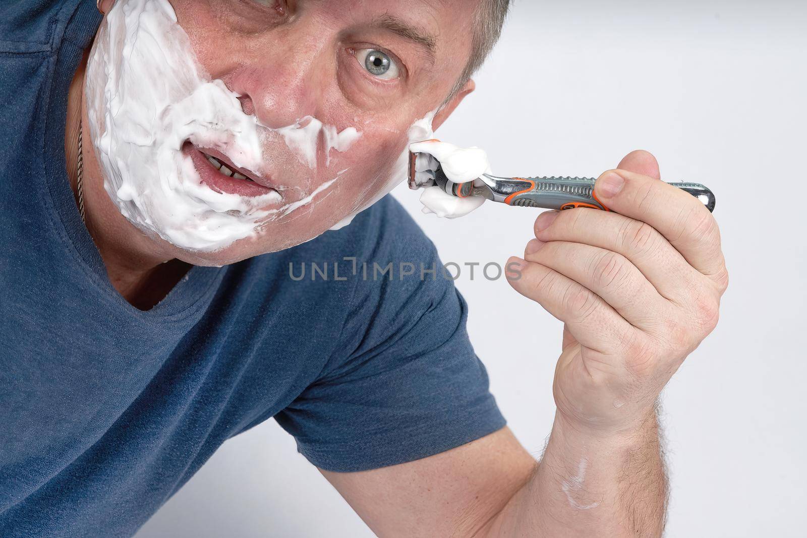 A man's face in shaving foam shaves with a safety razor. Morning or evening exercise, personal hygiene