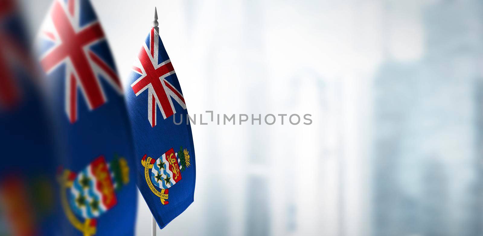 Small flags of Cayman Islands on a blurry background of the city.