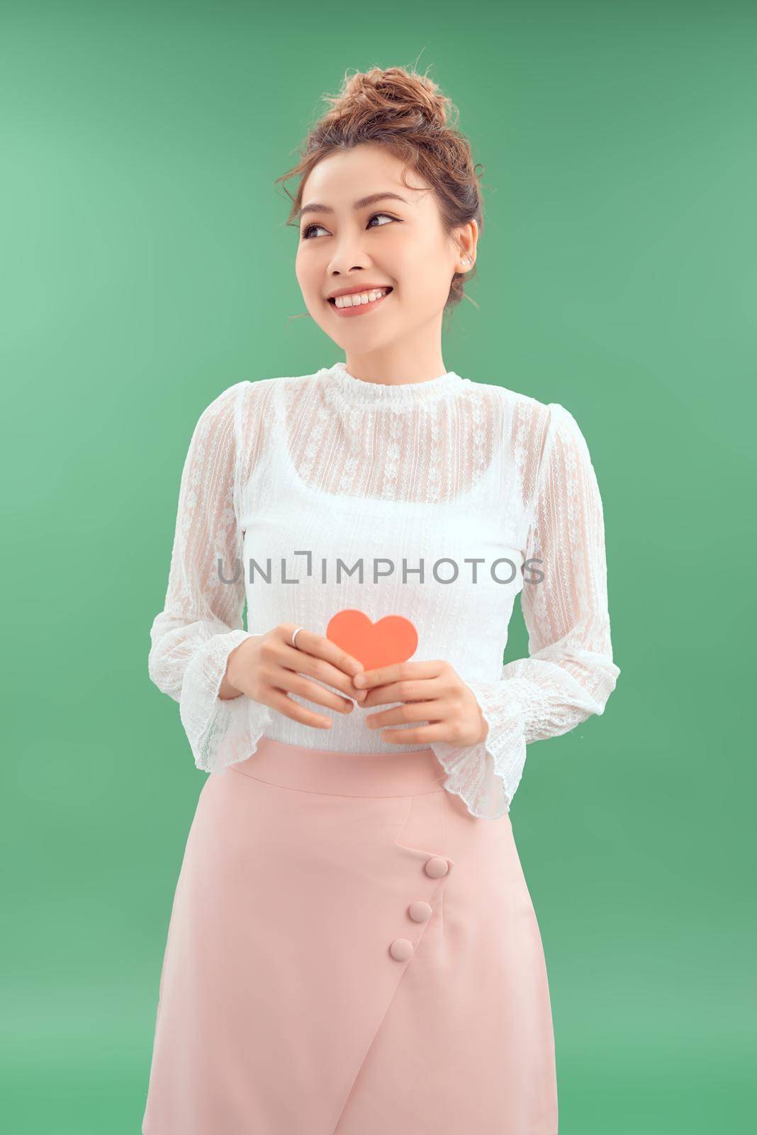 Attractive young Asian woman holding red heart in her hand over green background. by makidotvn