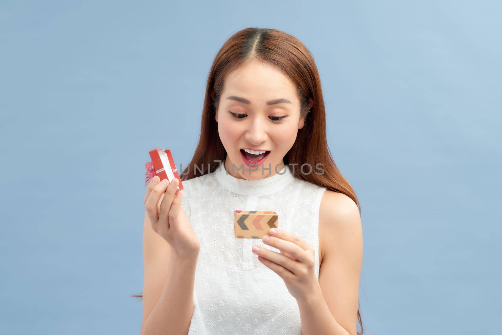 Cheerful young woman holding small gift box isolated on a blue background