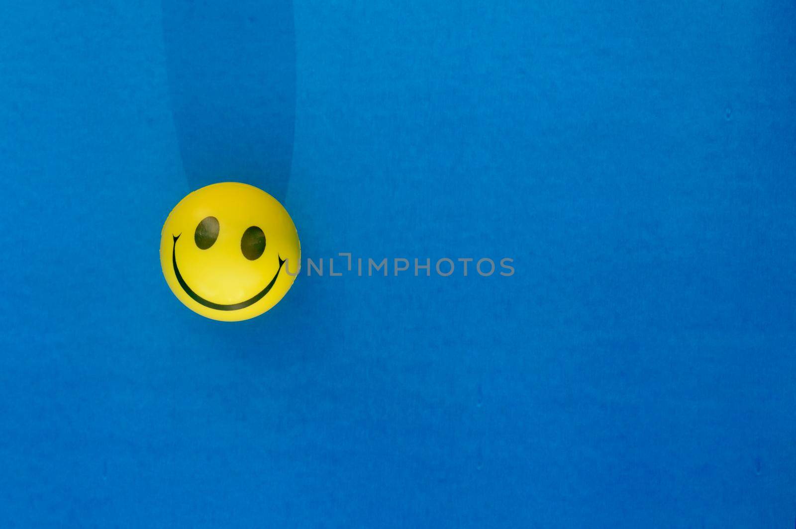 Anthropomorphic smiley face expression of a Squeeze Ball or Stress Ball isolated on blue background. Table top view. Close up. Happy smile background concept. by sudiptabhowmick