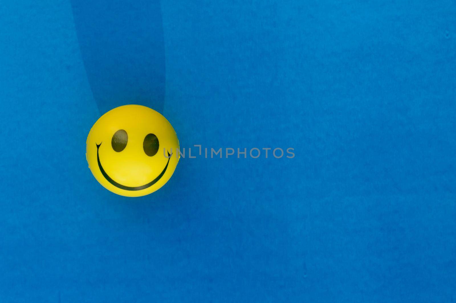 Anthropomorphic smiley face expression of a Squeeze Ball or Stress Ball isolated on blue background. Table top view. Close up. Happy smile background concept. by sudiptabhowmick