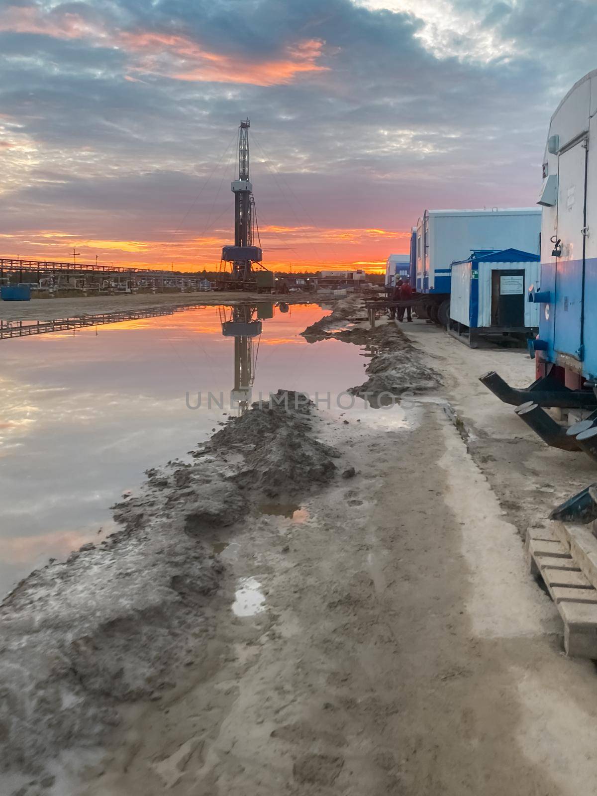 An oil field with an oil rig and wagons. Reflection in a puddle at sunset. Oil industry by levnat09