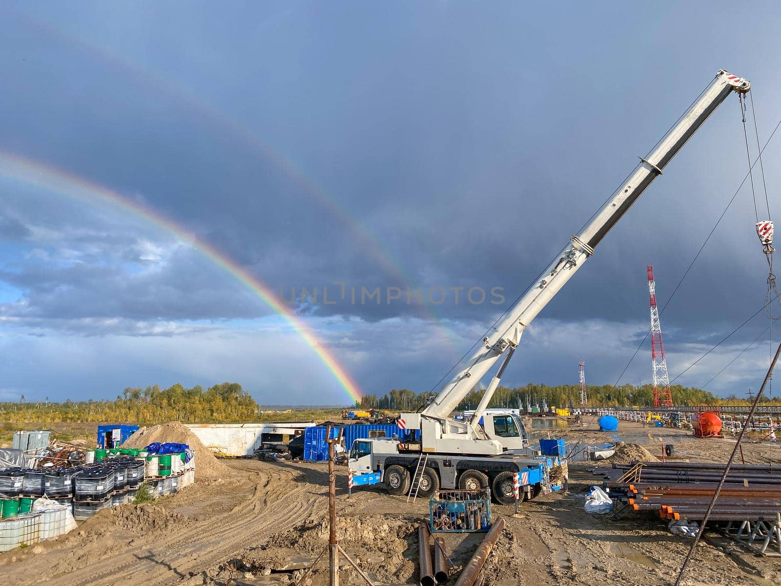 Oil field in the north, rainbow in the background. Working machines on the rig installation.