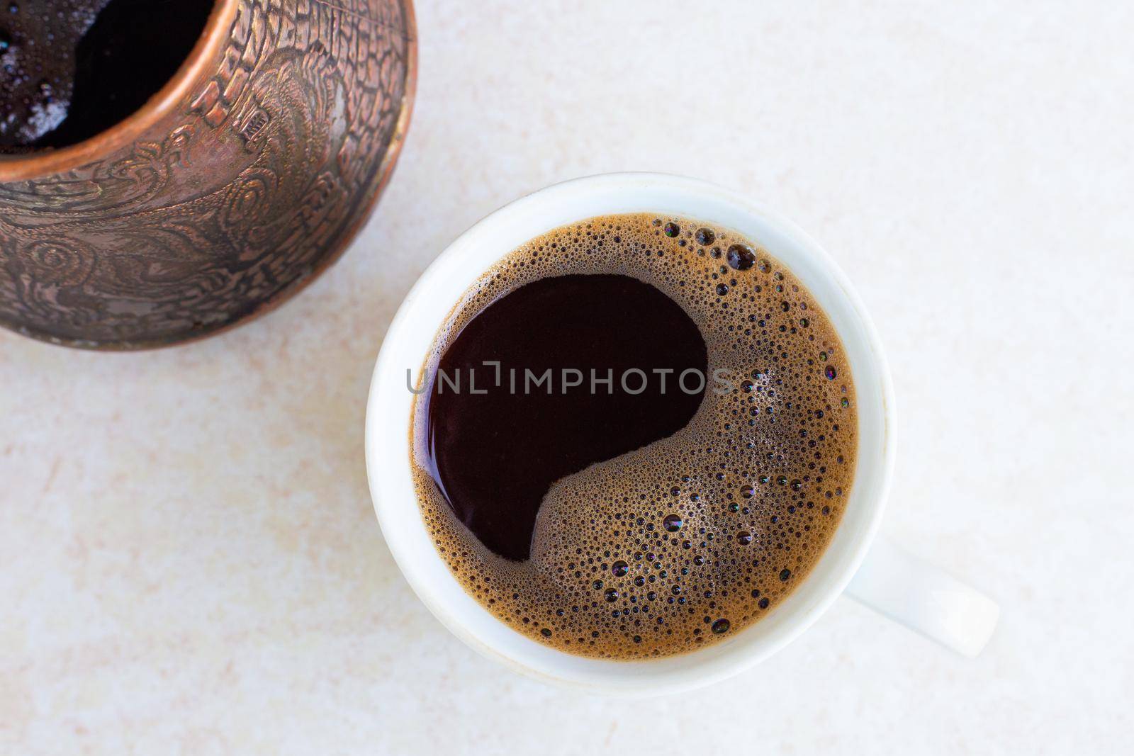 A mug and a Turk with freshly brewed coffee on a light table surface, top view. Morning awakening, the beginning of a new day. Strong invigorating drink.