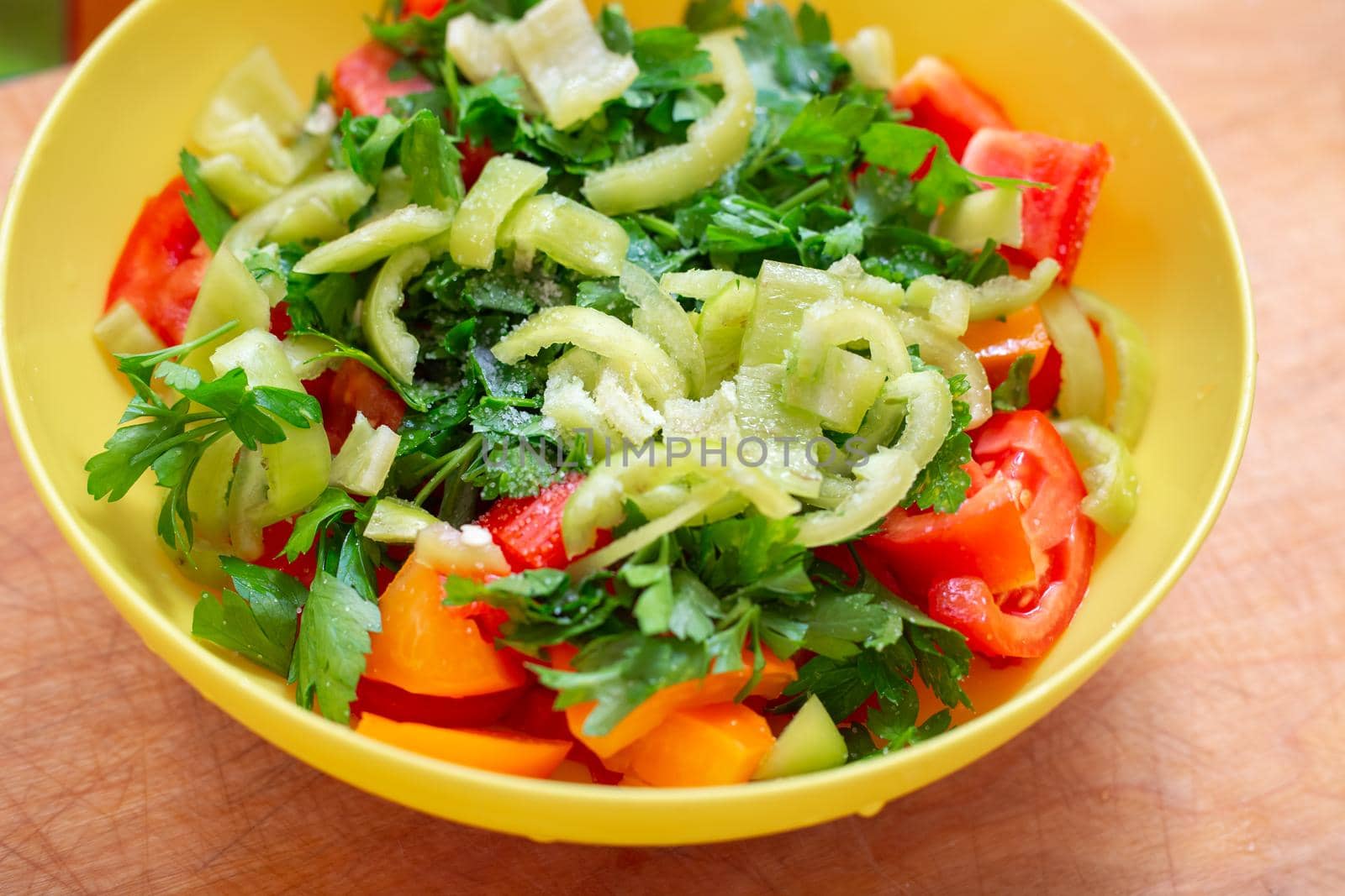 Vegetable salad with fresh tomatoes, peppers and parsley in a yellow cup. Delicious healthy snack.
