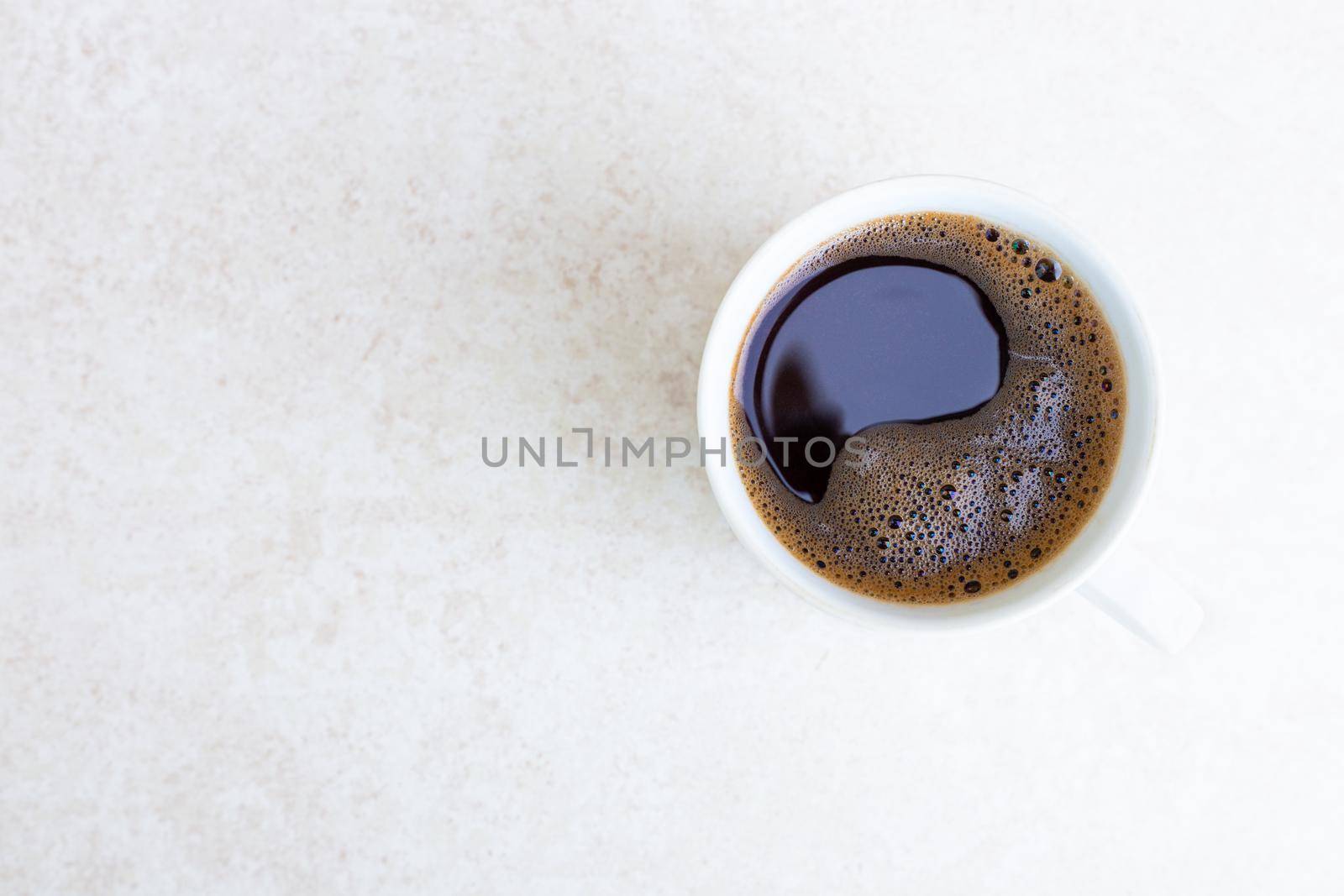 White mug with freshly brewed coffee on a light table surface with copy space, top view. Morning awakening, the beginning of a new day. Strong invigorating drink by levnat09