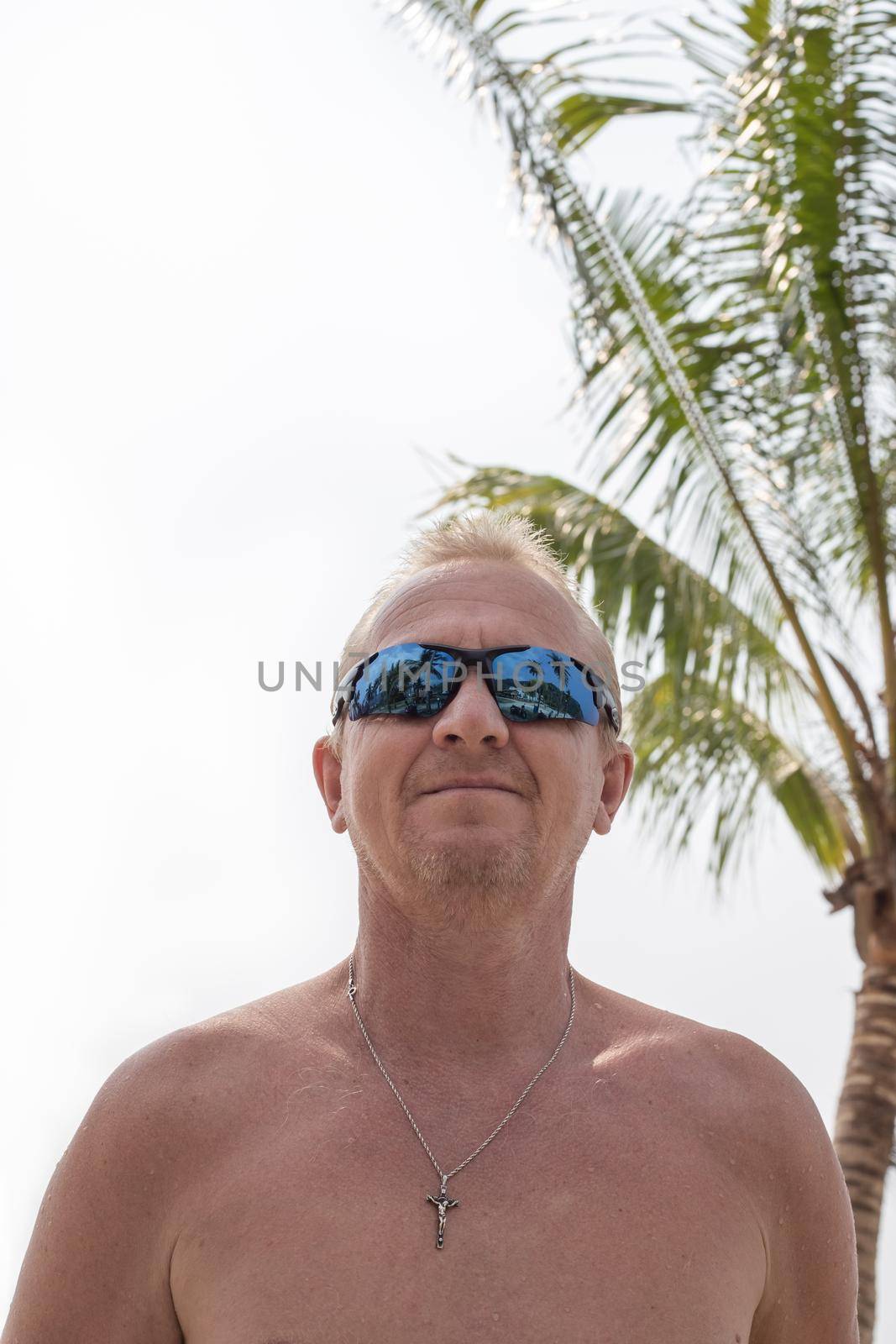 Caucasian man with a naked torso on a background of palm trees on a tropical island. Travel and tourism.