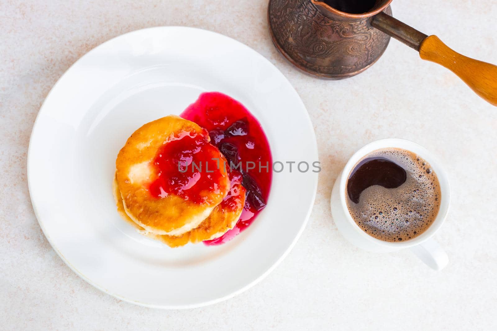 Fresh cheese cakes with plum jam and a mug with freshly brewed coffee on a light table top, top view. Wake up in the morning, start a new day. Hearty breakfast.