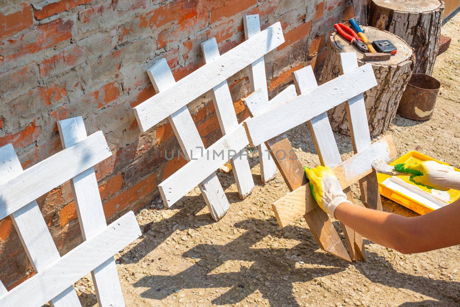 A woman paints a fence for a flower bed. Making and painting a decorative fence for a garden.