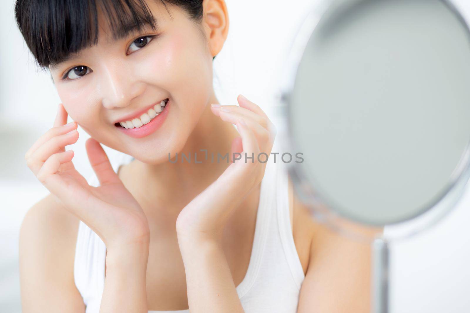 Beautiful face of young asian woman with happy smiling and touch cheek looking mirror with charming, makeup of beauty facial girl with skincare and cosmetic treatment, skin care and healthy concept.