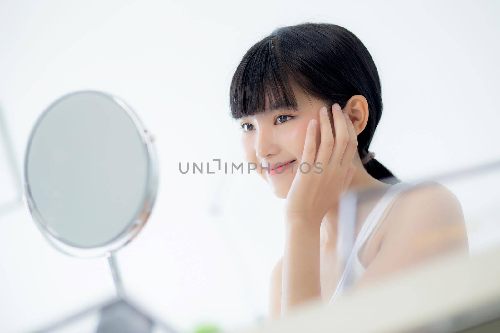 Beautiful face of young asian woman with happy smiling and touch cheek looking mirror with charming, makeup of beauty facial girl with skincare and cosmetic treatment, skin care and healthy concept. by nnudoo