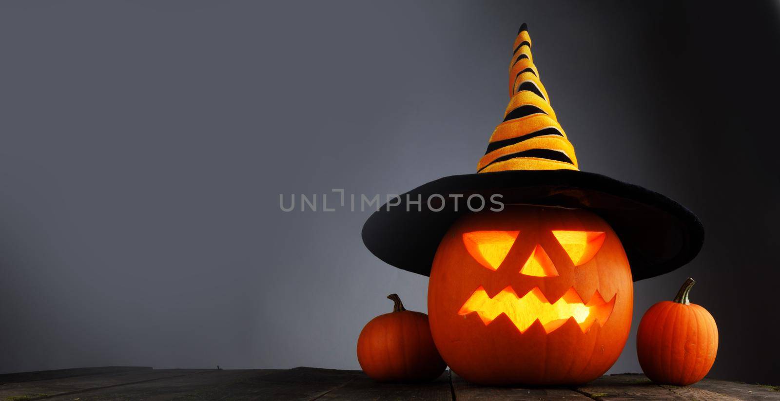 Jack O Lantern Halloween funny pumpkin with carved smiling face with witches hat on gray background with copy space for text
