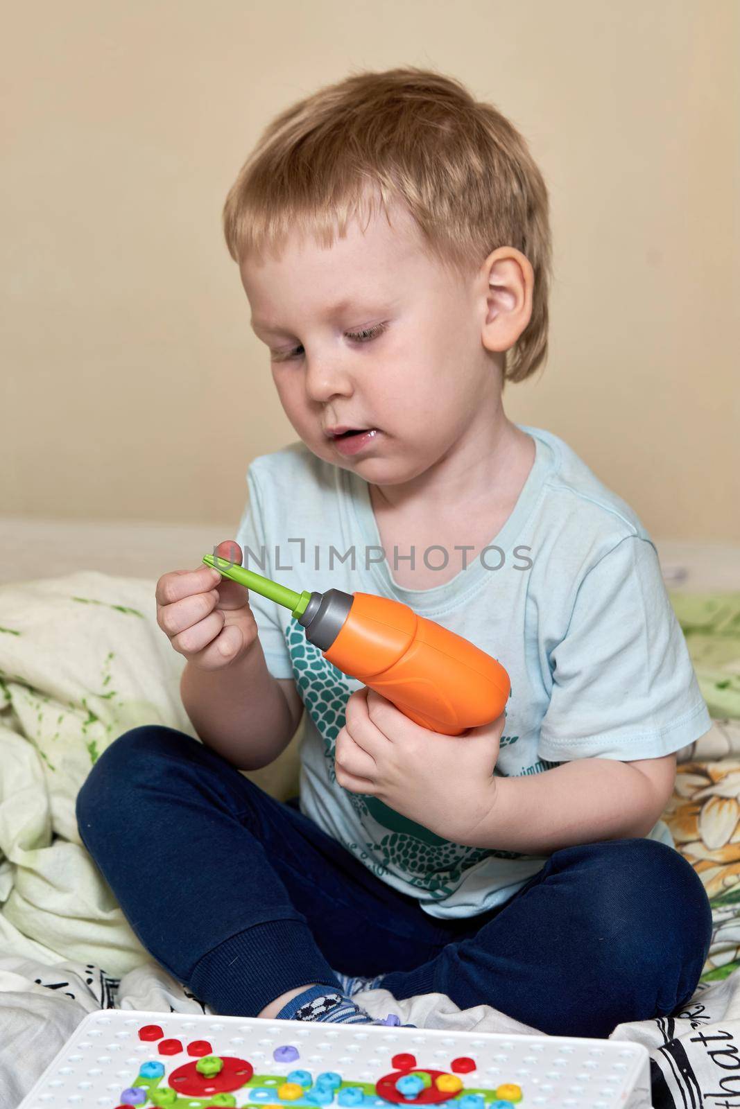 Vertical portrait of a child sitting cross-legged and playing with a toy screwdriver