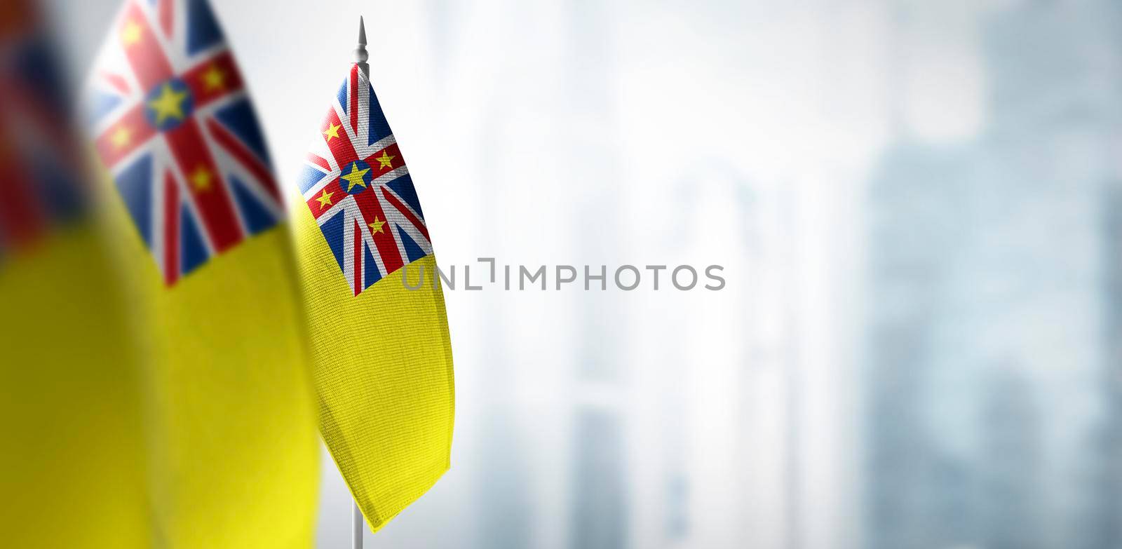 Small flags of Niue on a blurry background of the city.