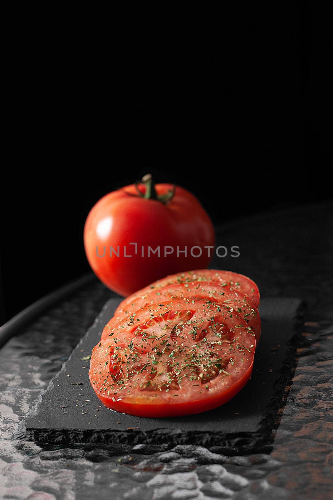 Sliced ​​and whole tomatoes with herbs. Black cutting board.