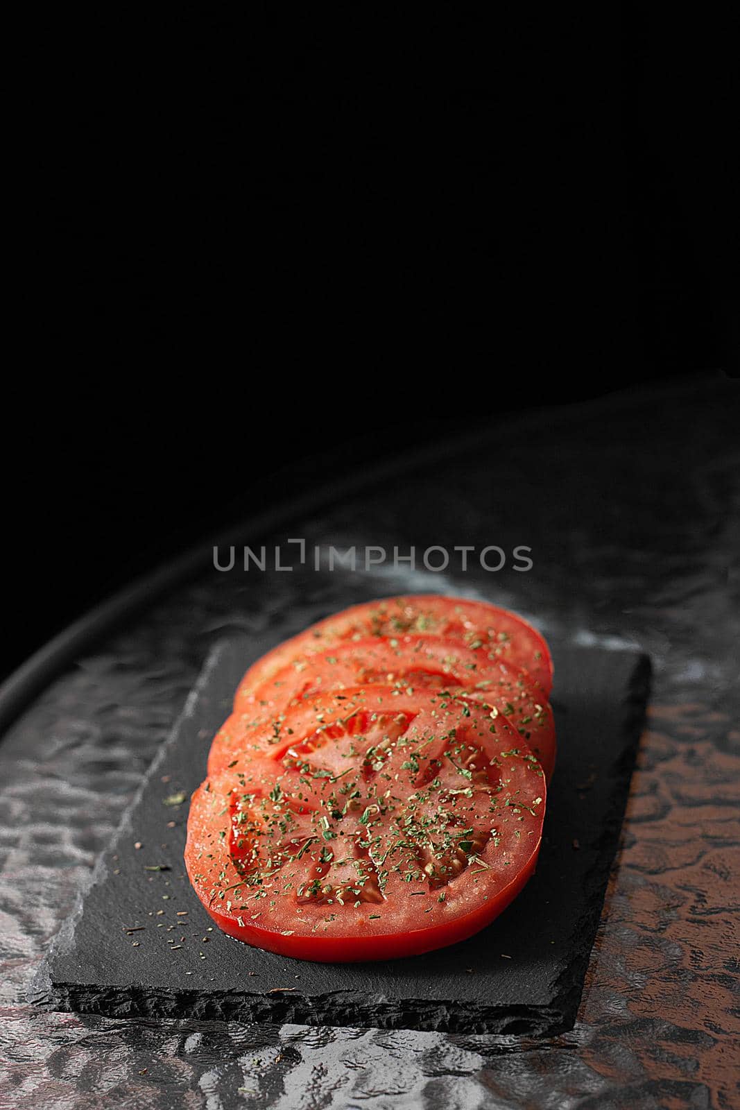 Sliced ​​tomatoes with herbs. Black cutting board.