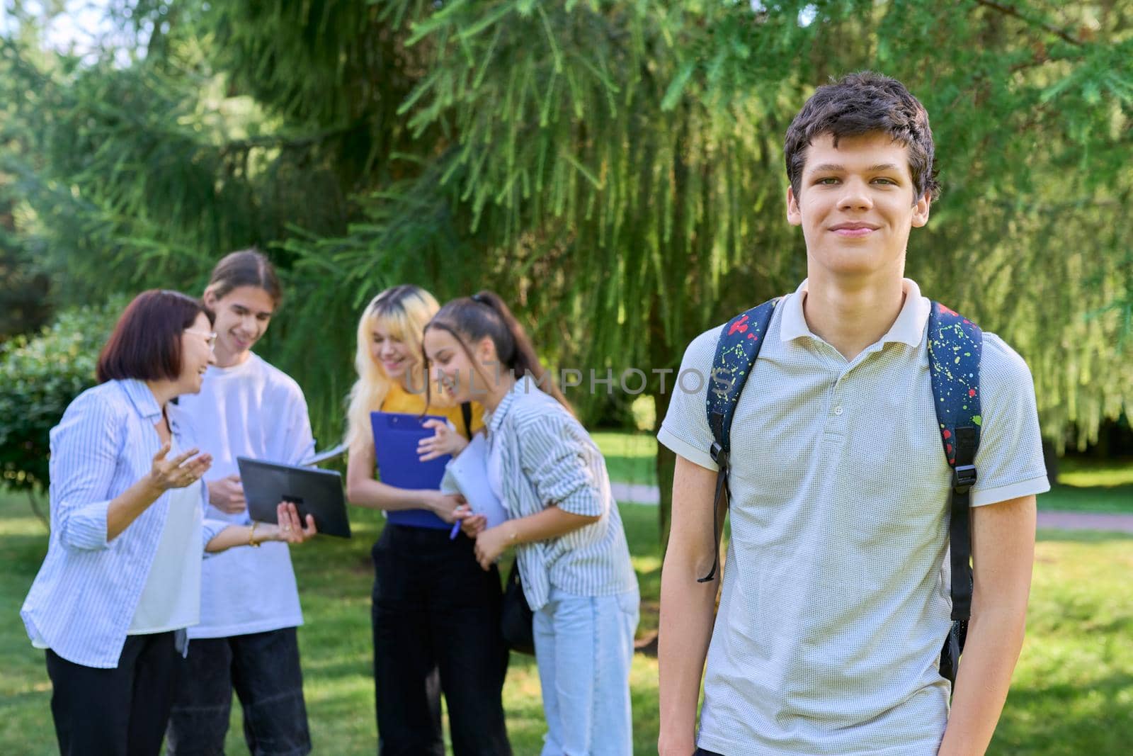 Portrait of male student in park campus, group of teenagers with teacher background. Adolescence, college, high school, education concept.