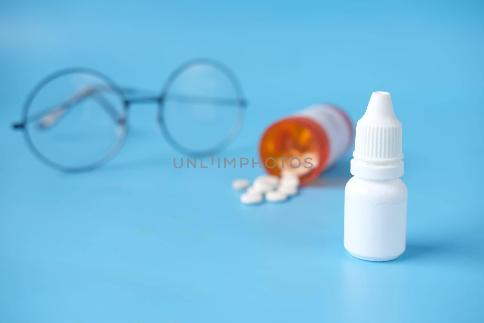 close up of eye drop bottle and eyeglass on white