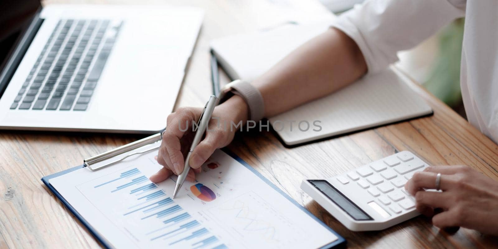 Close-up A businesswoman works on a financial chart report, calculates business costs and profits, and sits at her desk. by wichayada