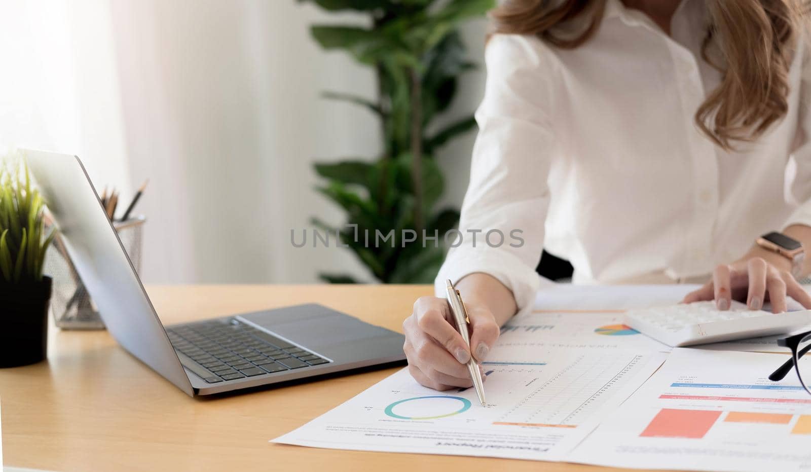 The hand of Asian woman is pressing calculator and prepare information for report to correct. While still holding a silver pen in finger. When calculated completed, can be recorded immediately..