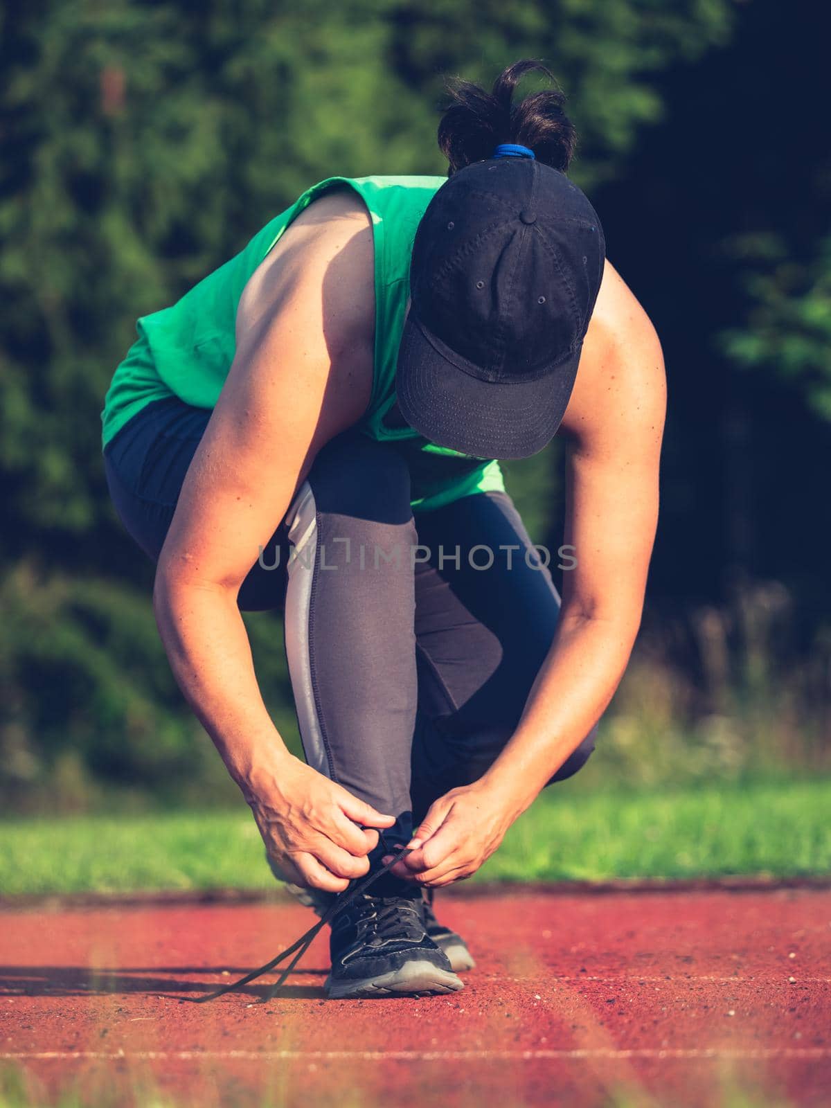 Young fit girl runner tying shoelaces. Athletic woman on red running stadium track