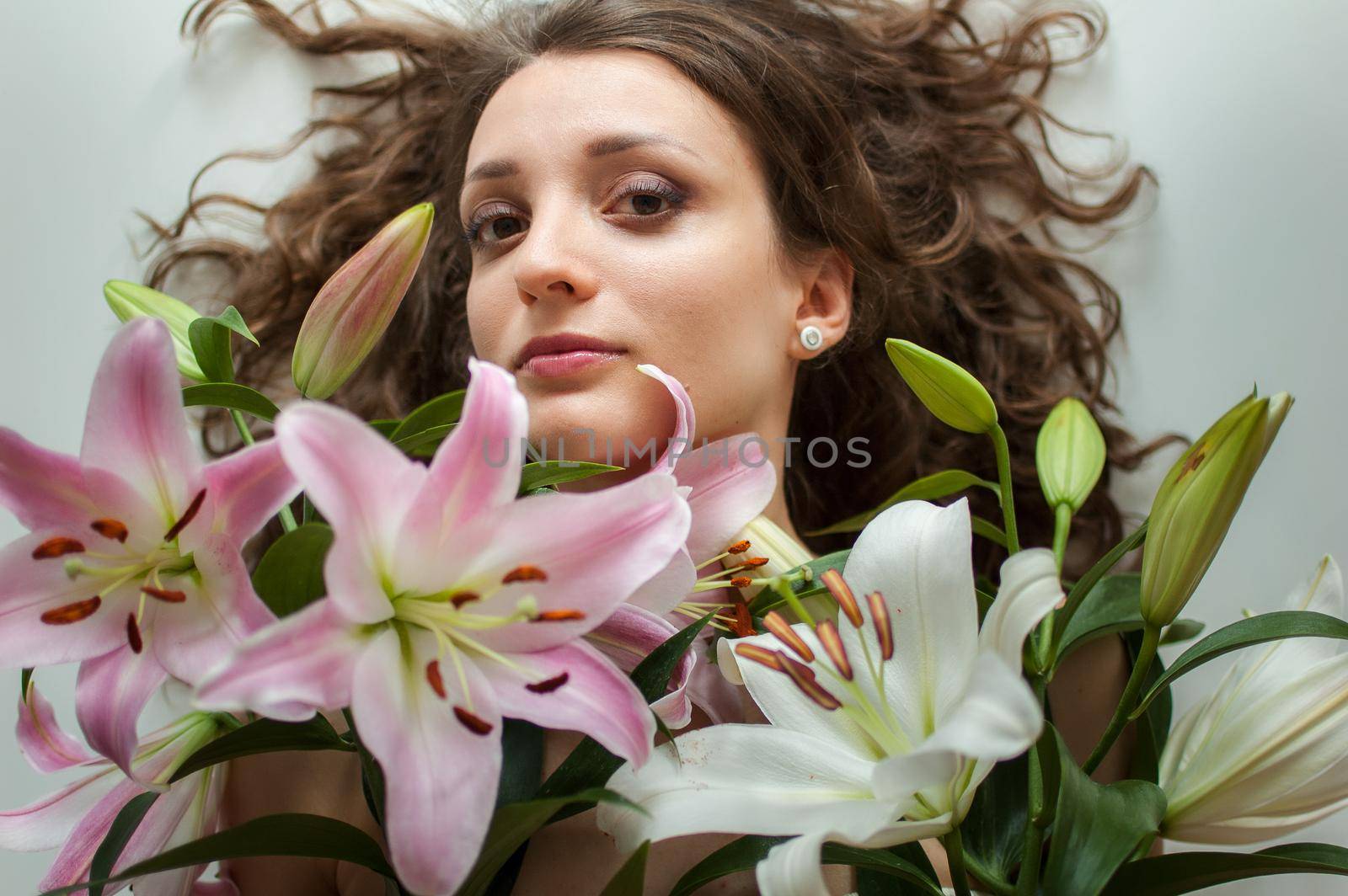 Top view of beautiful woman lying on the table with perfect bouquet of beautiful lilies, female portrait concept.