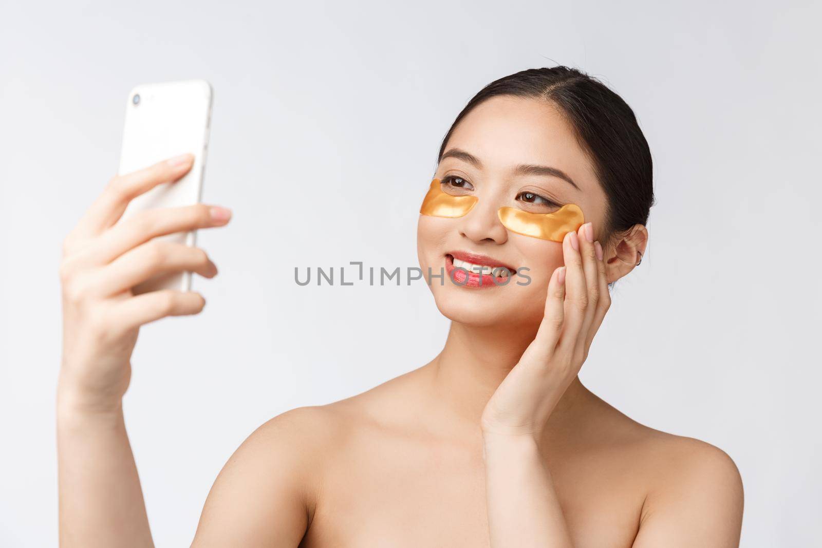 Close up selfie of beautiful happy woman with eye mask on face.Woman with eyes mask taking selfie with mobile phone at home enjoying relaxation.