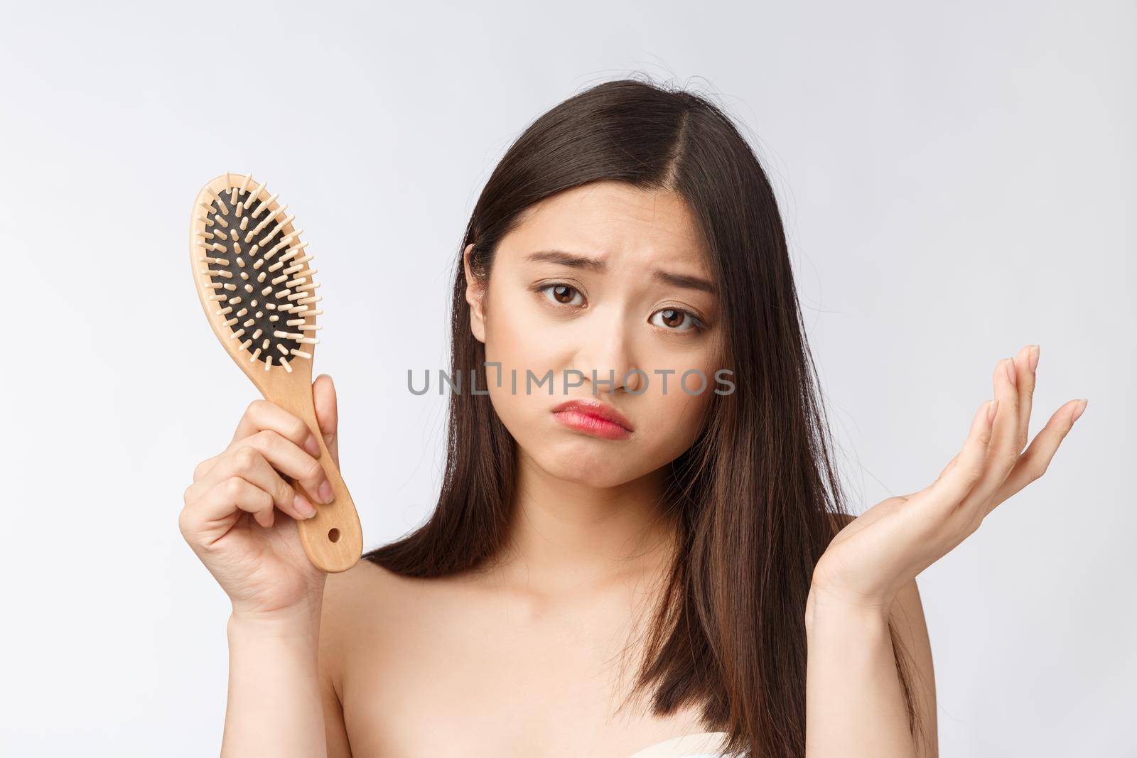 Upset stressed young Asian woman holding damaged dry hair on hands over white isolated background