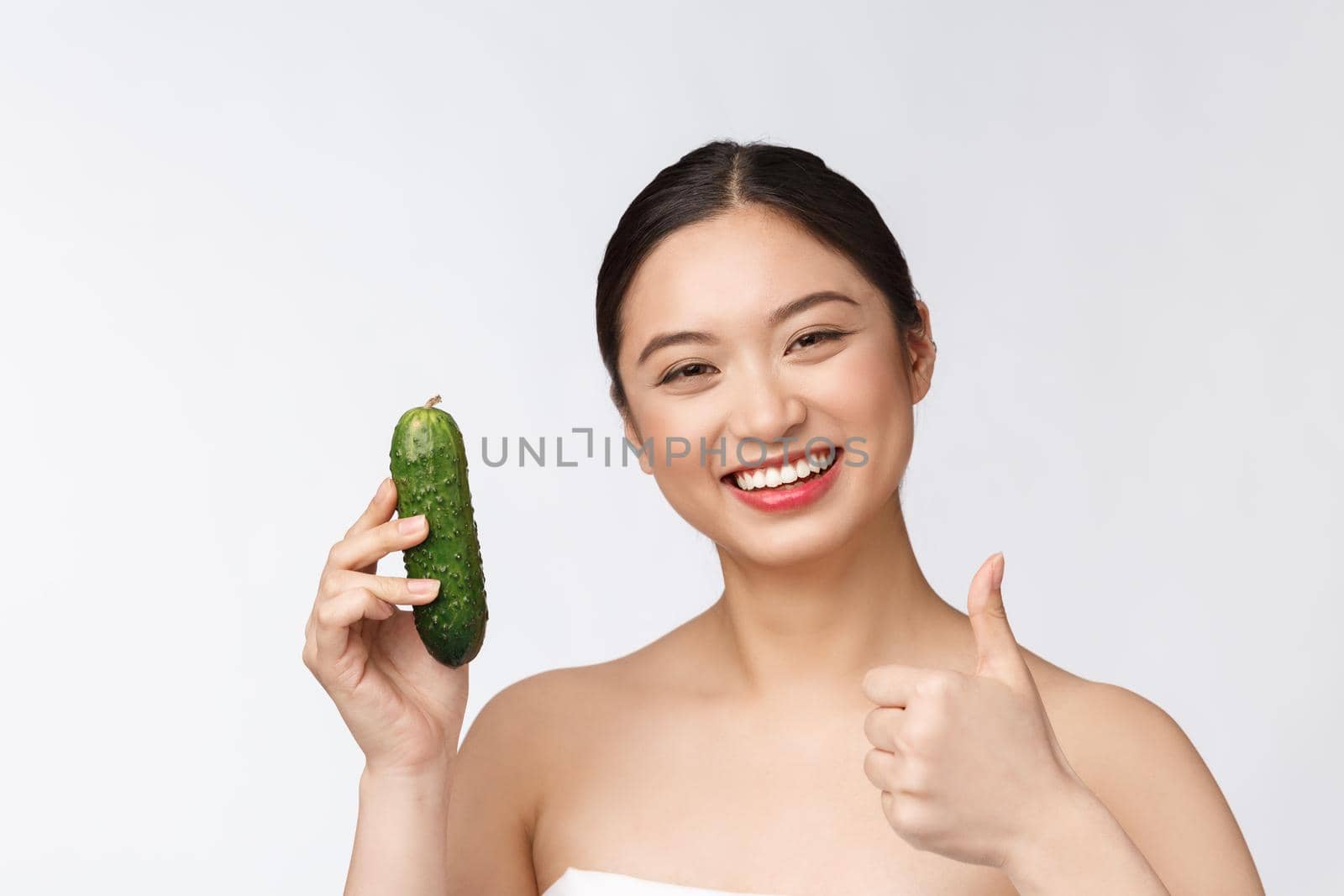Asian young woman over isolated background holding cucumber. by Benzoix