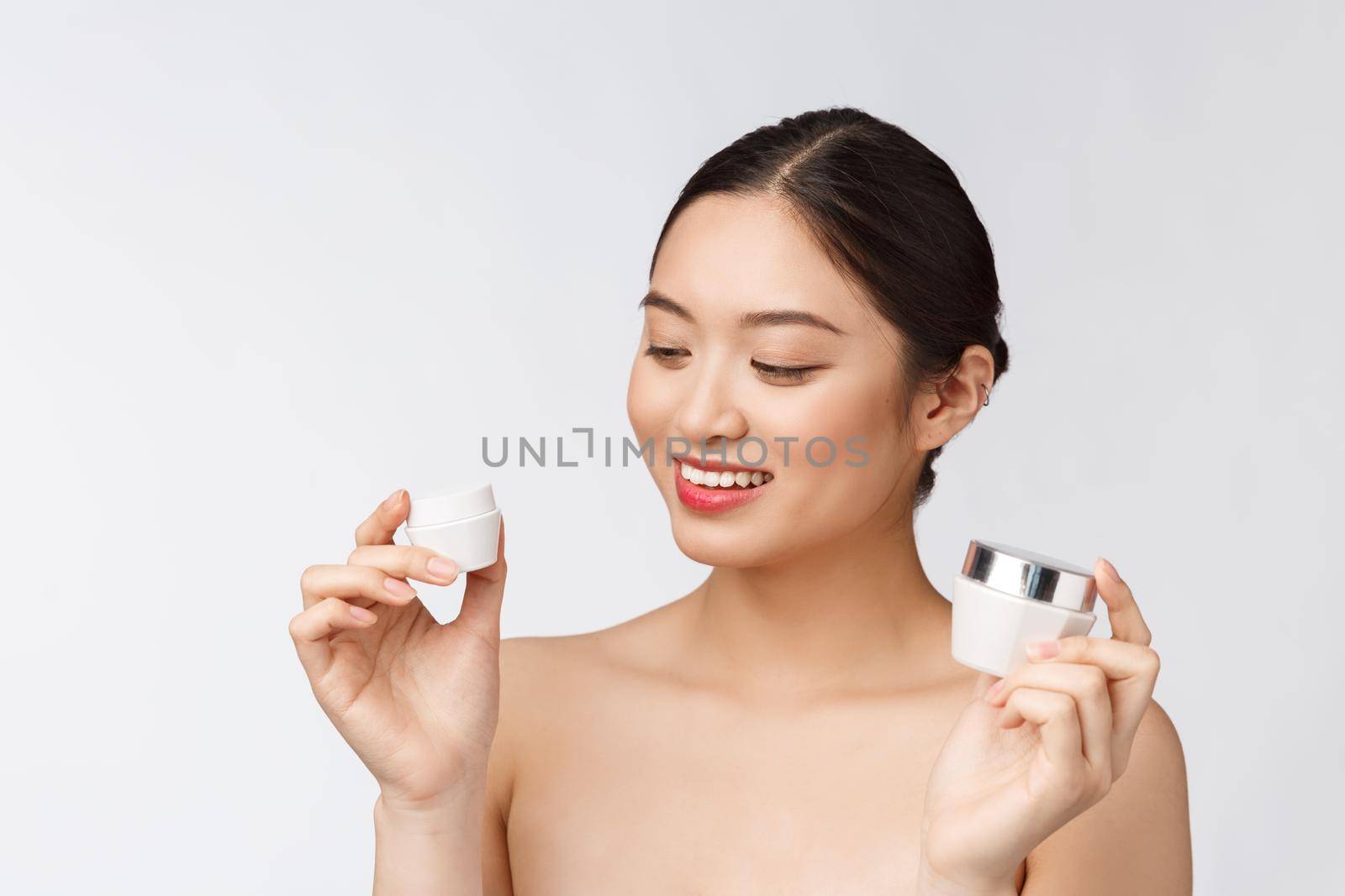 Beautiful young woman on white isolated background holding cosmetic face cream, asian.