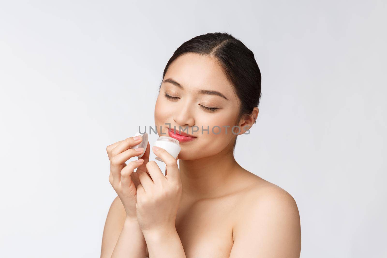 Beautiful young woman on white isolated background holding cosmetic face cream, asian.