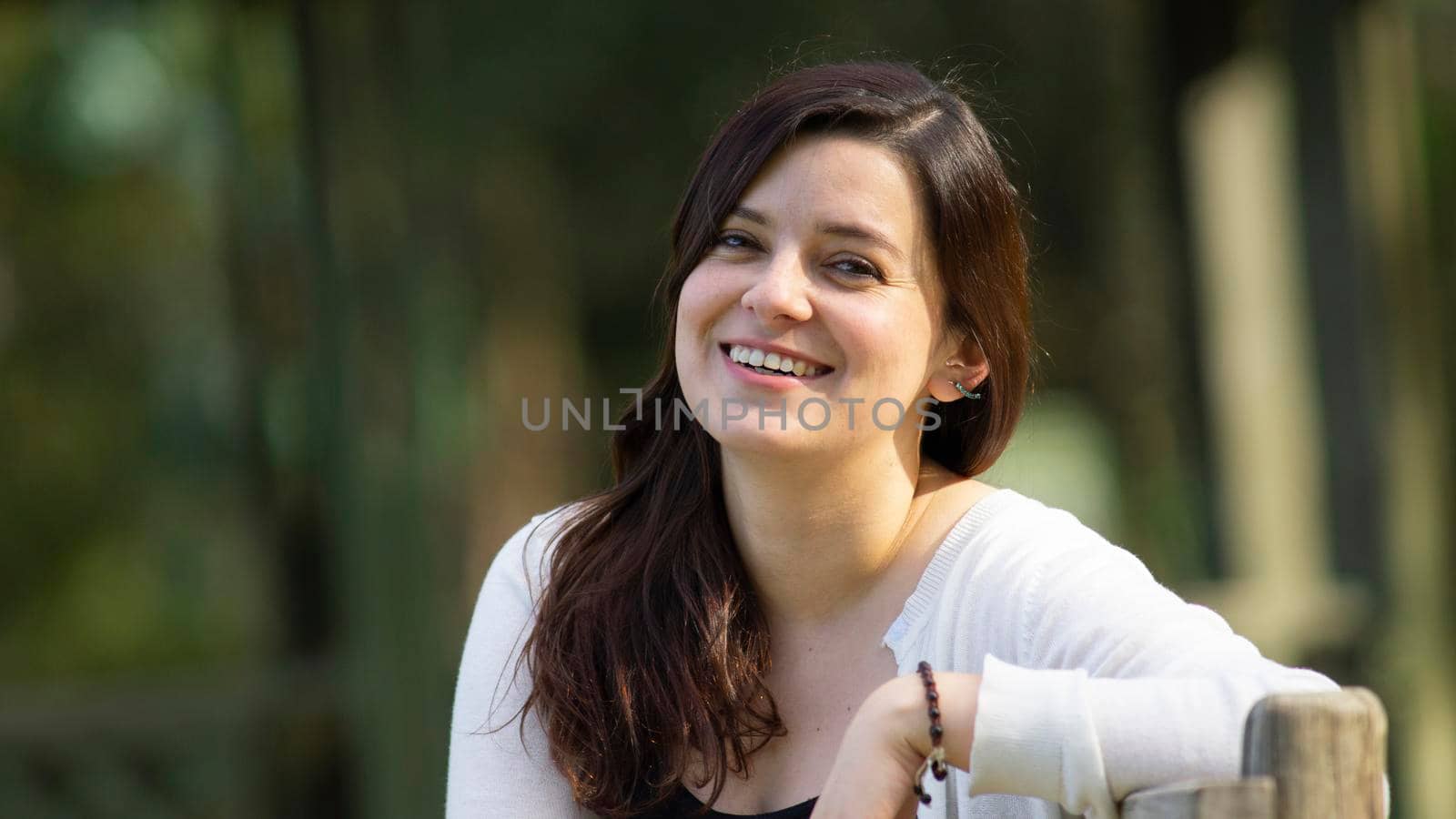 Portrait of a beautiful young Hispanic woman in the middle of a park with a very cheerful attitude against a background of unfocused green trees by alejomiranda
