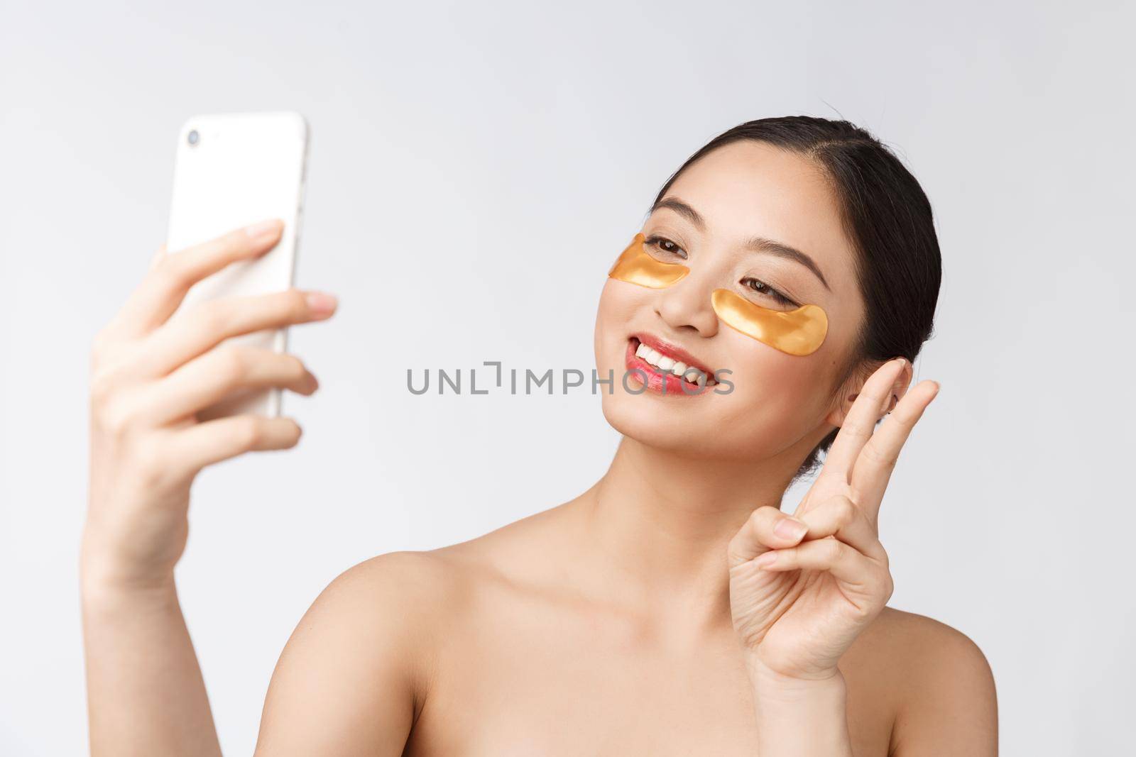 Close up selfie of beautiful happy woman with eye mask on face.Woman with eyes mask taking selfie with mobile phone at home enjoying relaxation.
