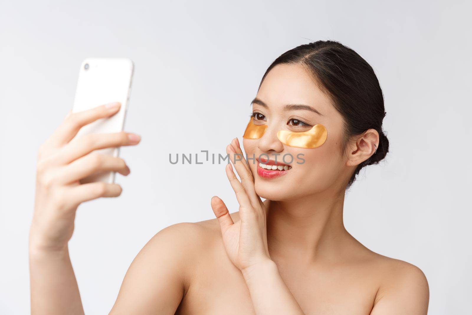 Close up selfie of beautiful happy woman with eye mask on face.Woman with eyes mask taking selfie with mobile phone at home enjoying relaxation.